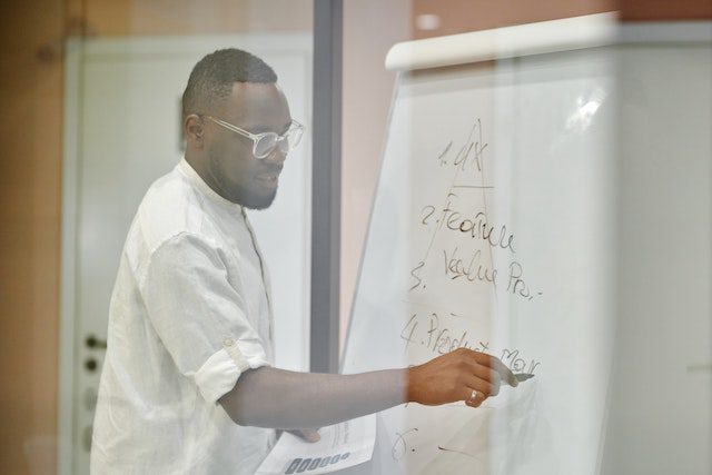 Photo of a Man in a White Dress Shirt Writing on a Whiteboard