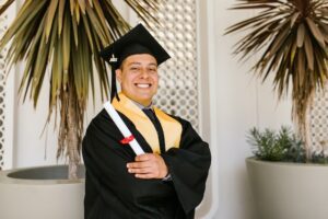 Proud Man Smiling Wearing Graduation Gown And Holding His Diploma