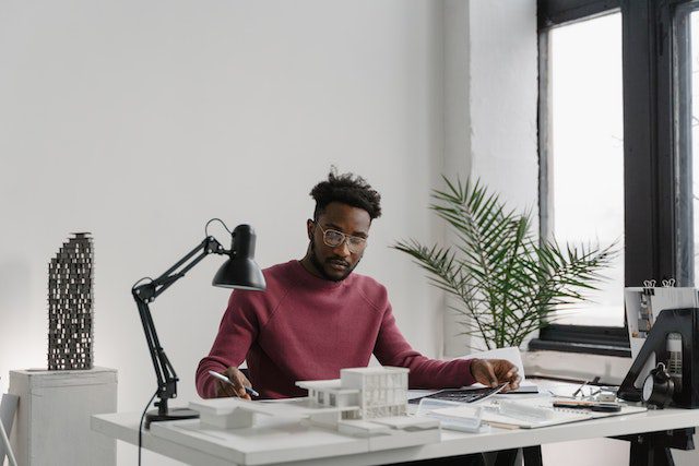 Man in Pink Sweater Sitting on a Chair Behind His Desk