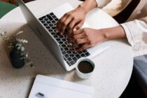 Person Using Macbook Pro Beside White Ceramic Mug