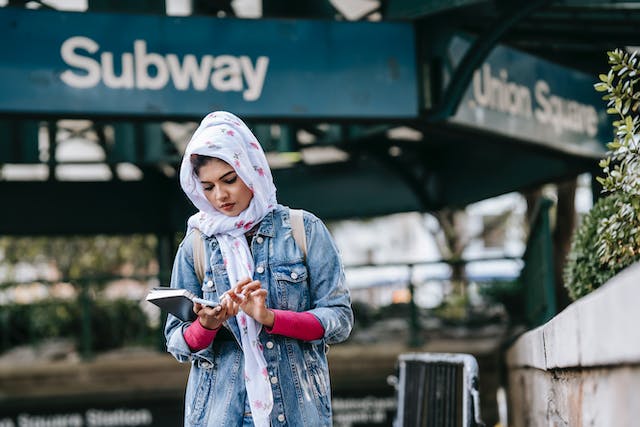 serious ethnic woman messaging via smartphone while standing near subway