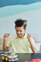 a happy boy in yellow polo shirt looking at the toy on the table