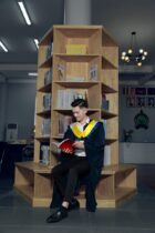 a man in a graduation gown sitting on a shelf