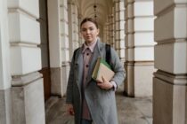 a woman in a gray coat holding books