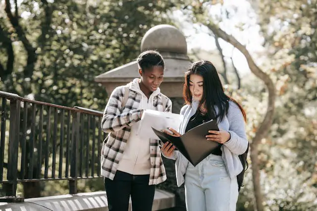 diverse female students with folders discussing homework in urban park