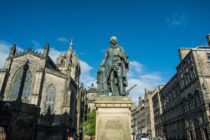 man in coat statue near buildings