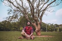 man in red polo shirt sitting on green grass field near a bare tree