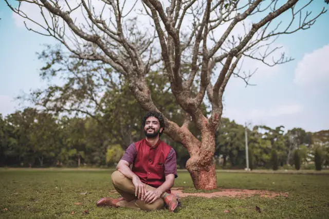 man in red polo shirt sitting on green grass field near a bare tree