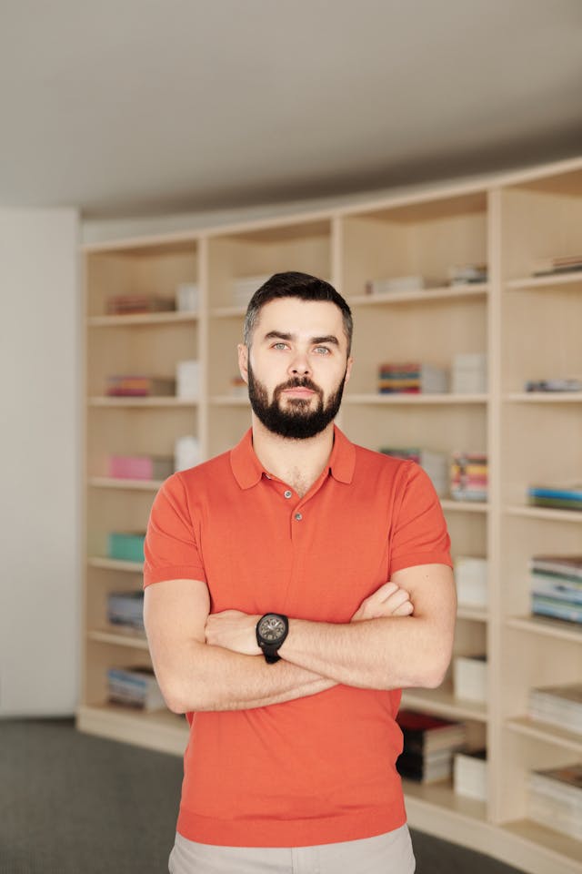 portrait of man wearing orange polo shirt in a library