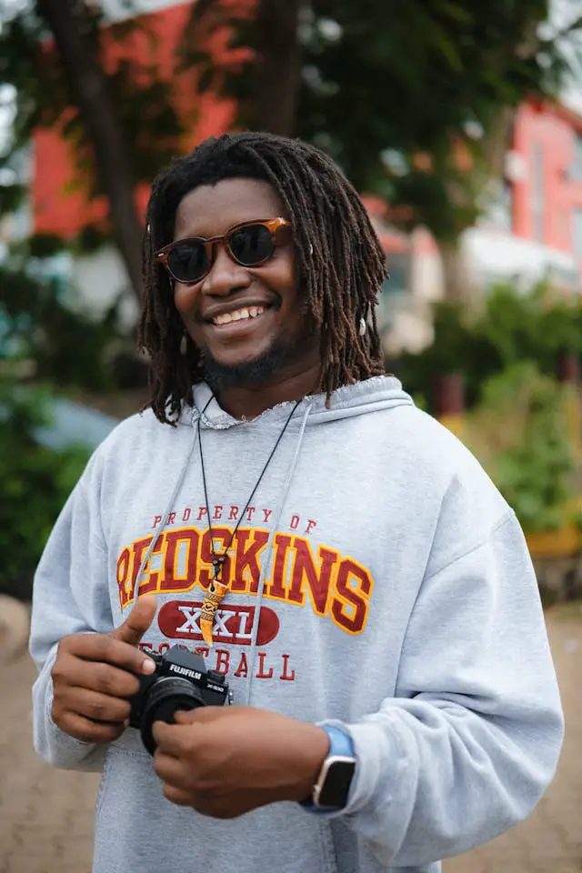 smiling man with dreadlocks holding camera outdoors