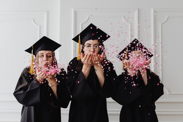 women wearing graduation caps blowing confetti