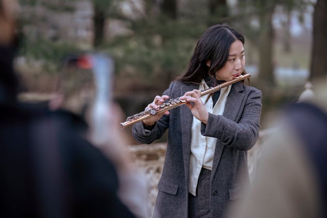 man in a gray suit playing flute in a park