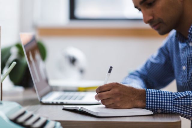 person writing notes beside laptop