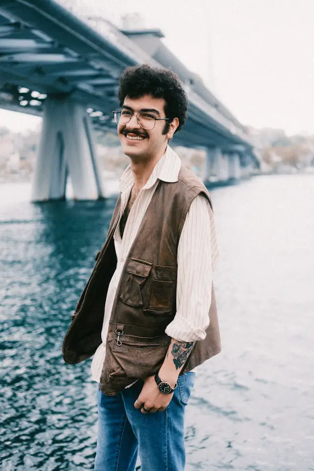 smiling man posing by water under bridge