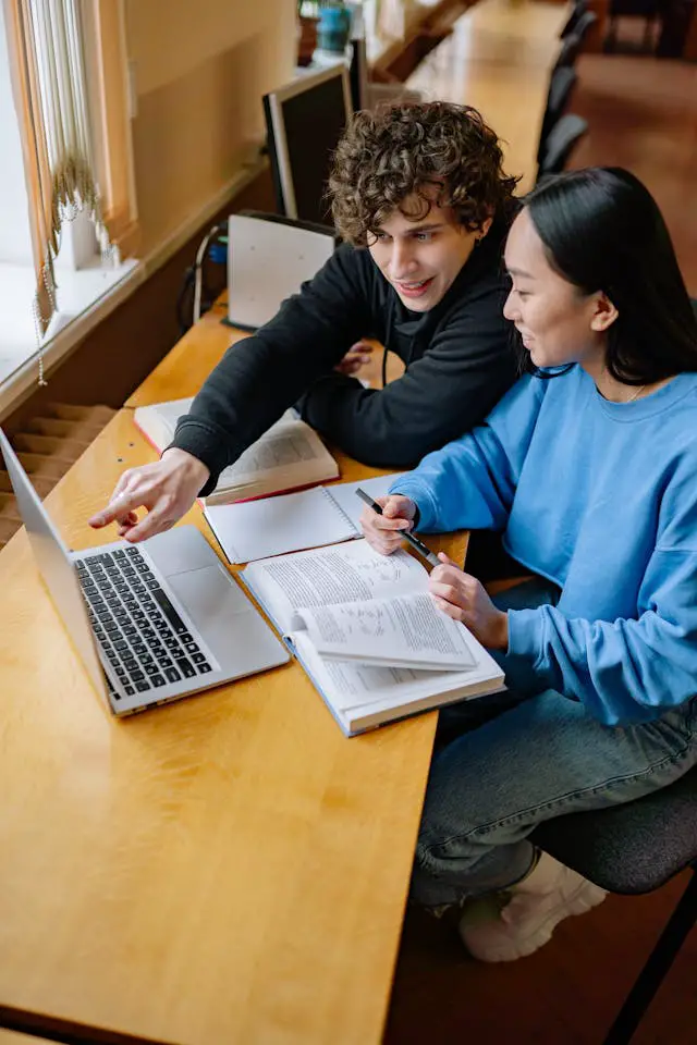 students sitting at the desk in a library and looking at a laptop screen