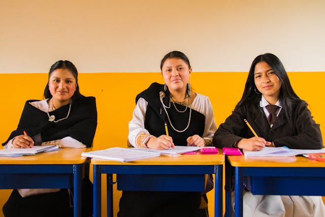 teacher and schoolgirls sitting by tables