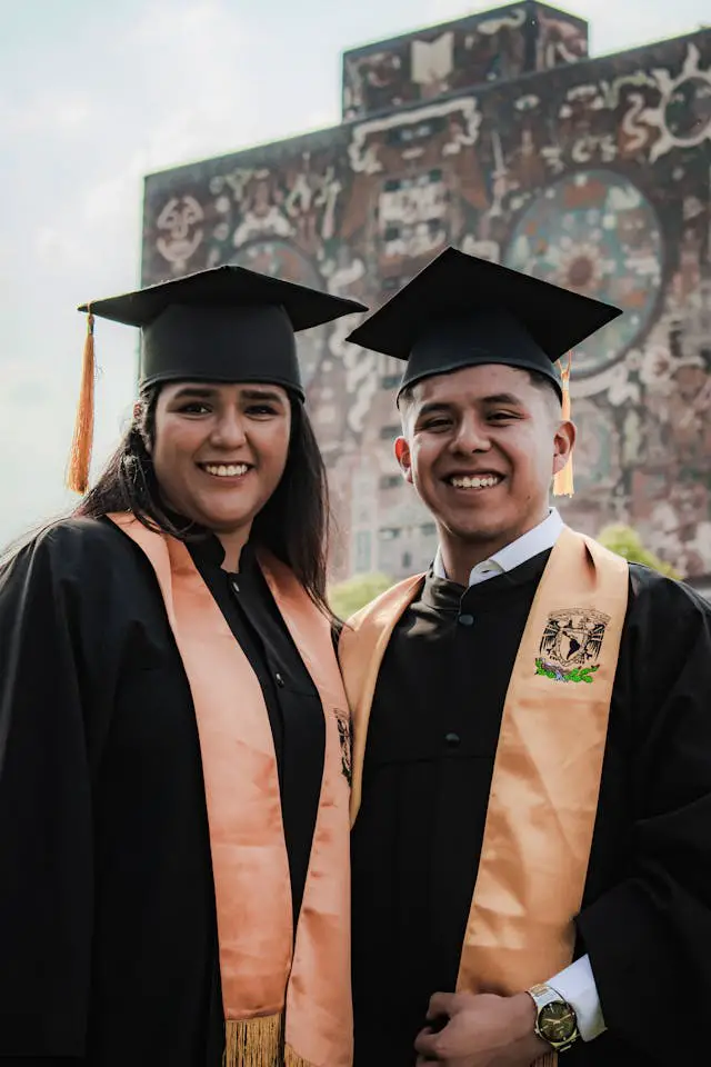 young woman and man standing wearing graduation gowns at university campus