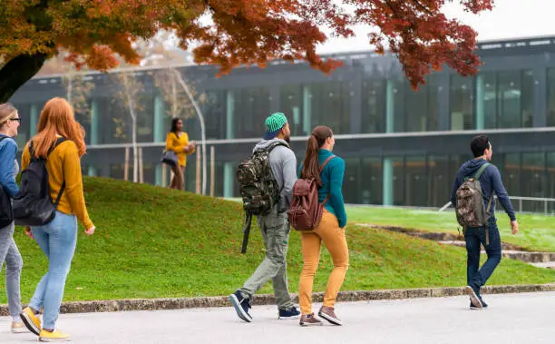 Group of students walking and standing in front of a modern glass university building