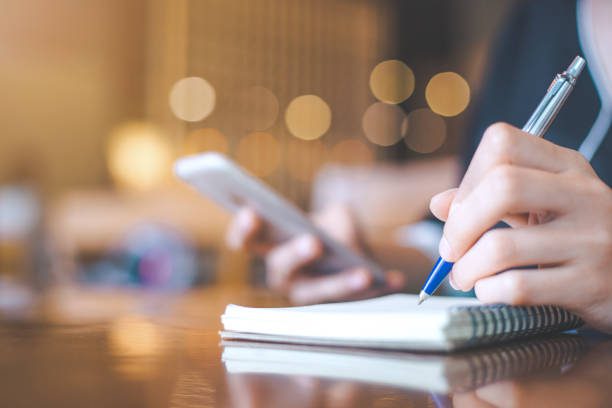 Business woman hand is on a notepad with a pen on a wooden desk in the office.