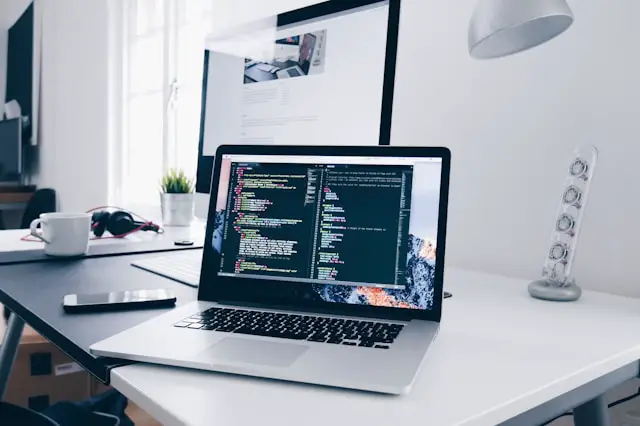 a macbook with lines of code on its screen on a busy desk