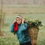 woman in teal jacket carrying woven basket full of leaves