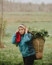 woman in teal jacket carrying woven basket full of leaves