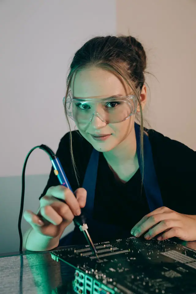 close up shot of a woman holding a soldering iron while wearing protective goggles