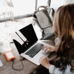 girl wearing grey long sleeved shirt using macbook pro on brown wooden table