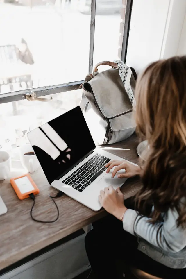 girl wearing grey long sleeved shirt using macbook pro on brown wooden table