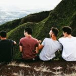 row of four men sitting on mountain trail