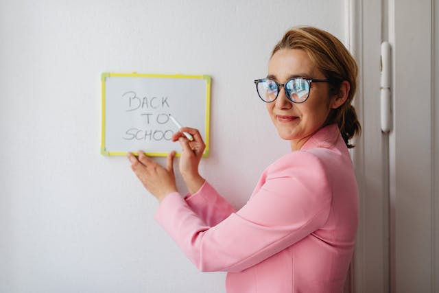 smiling woman in pink blazer holding a whiteboard with back to school text