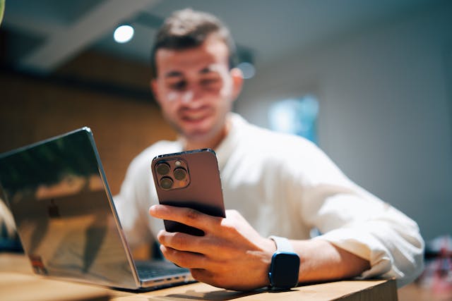 a man sitting at the desk and using a laptop and smartphone