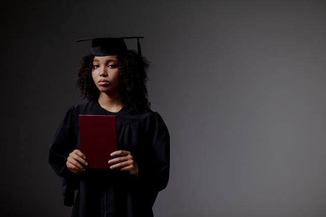 a woman in academic regalia holding a red book