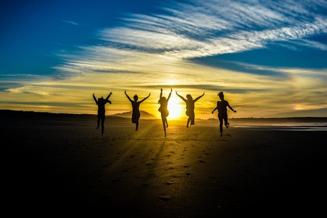 people jumping on shore front of golden hour